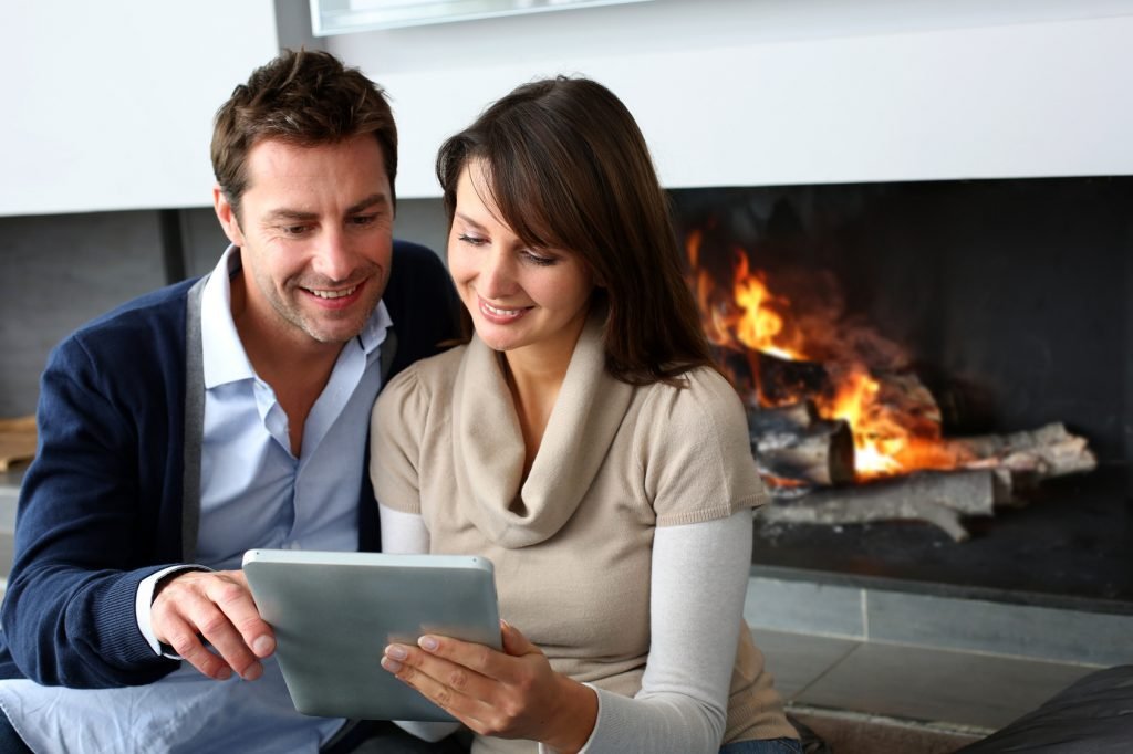 Couple sitting by fireplace and websurfing with tablet