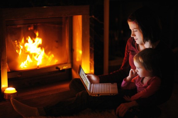 Young mother and daughter by a fireplace with a laptop